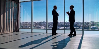 两个人的商务谈话。穿着西装的企业家在宽敞的办公室里谈生意，背景是窗户。