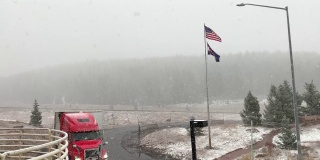 在一个多雪、多雾的日子里，一辆半挂车驶过悬挂着美国国旗和科罗拉多州国旗的Vail Pass，这是沿70号州际公路的科罗拉多山山顶的一个休息站