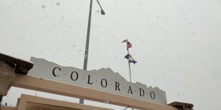 前景中的科罗拉多信息标志，作为美国国旗和科罗拉多州旗在韦尔垭口的风中飘扬，在一个多雪、多雾的日子里，沿着70号州际公路的科罗拉多山山顶的休息站