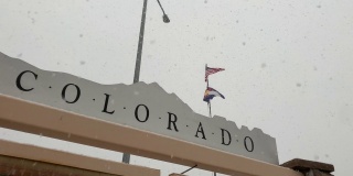 揭示镜头从一个科罗拉多信息标志摇到美国国旗和科罗拉多州旗在韦尔垭口的风中飞行，在一个雪天，雾天沿州际公路70号科罗拉多山的山顶休息站