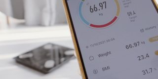 成年人的手在家里用智能手机检查体重，健康的生活方式理念。