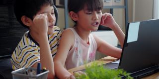 亚洲兄妹在家里用笔记本电脑玩网络游戏的时候聊天。维系和分享爱的家庭