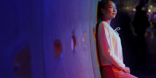 年轻的亚洲妇女走在城市街道霓虹灯照明晚上的4K肖像。