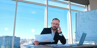 在办公室工作的严肃的商人。穿着西装的大胡子老板坐在办公桌前，拿着笔记本电脑打电话。经营理念。