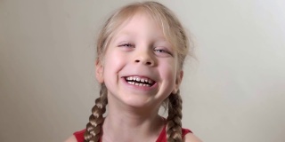 一个5岁的小女孩的特写肖像，蓝色的大眼睛，金发，2个辫子的发型，美丽甜美的微笑。孩子开心地笑着，笑着。面部表情和情绪。
