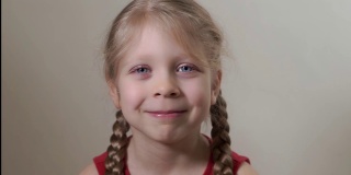 一个快乐的女孩的肖像接近蓝色的大眼睛，金发，2辫子的发型，美丽可爱的微笑。孩子开心地笑着，笑着。面部表情和情绪。