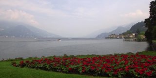 科莫湖岸边的贝拉吉奥岛充满浪漫气息。前景是红色的花朵，背景是云层中的意大利阿尔卑斯山。轻松的气氛。