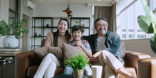 幸福甜蜜的亚洲家庭，爸爸妈妈和儿子一起坐在沙发上看电视。笑着微笑的亚洲家庭在家里隔离隔离时刻处于封锁状态。