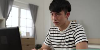 被隔离在卧室的亚洲男学生在家里用笔记本电脑观看视频讲座时，眼睛受到了刺激，正在揉眼睛
