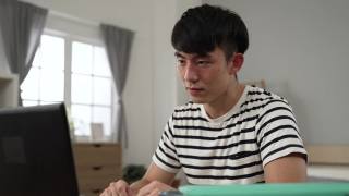被隔离在卧室的亚洲男学生在家里用笔记本电脑观看视频讲座时，眼睛受到了刺激，正在揉眼睛视频素材模板下载