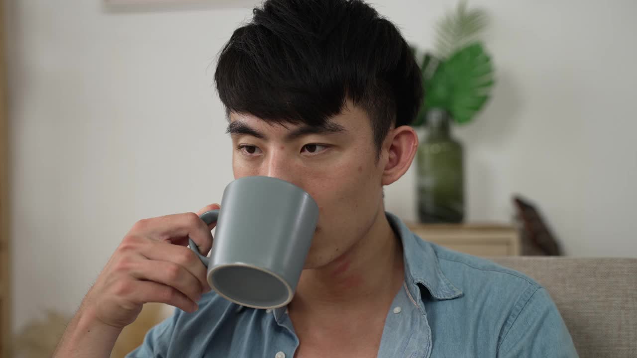 一名沮丧的亚洲年轻男性一边喝茶一边绝望地望着远方，一边对封锁期间的失业感到非常焦虑。