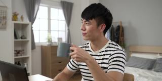 侧面的照片中，一位穿着休闲服装在家工作的中国男性，在卧室里享受着早晨的咖啡，面带微笑地望着远方