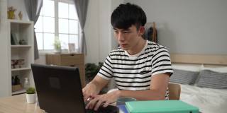 有压力的亚洲学生在家学习，困惑和惊讶的数据突然丢失时，在卧室的笔记本电脑上打字报告。