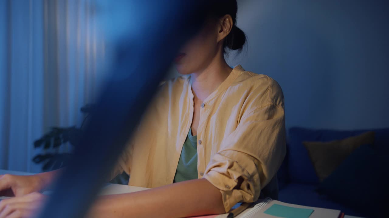 亚洲职业女性，穿着休闲服装，晚上在家里客厅用笔记本电脑工作。