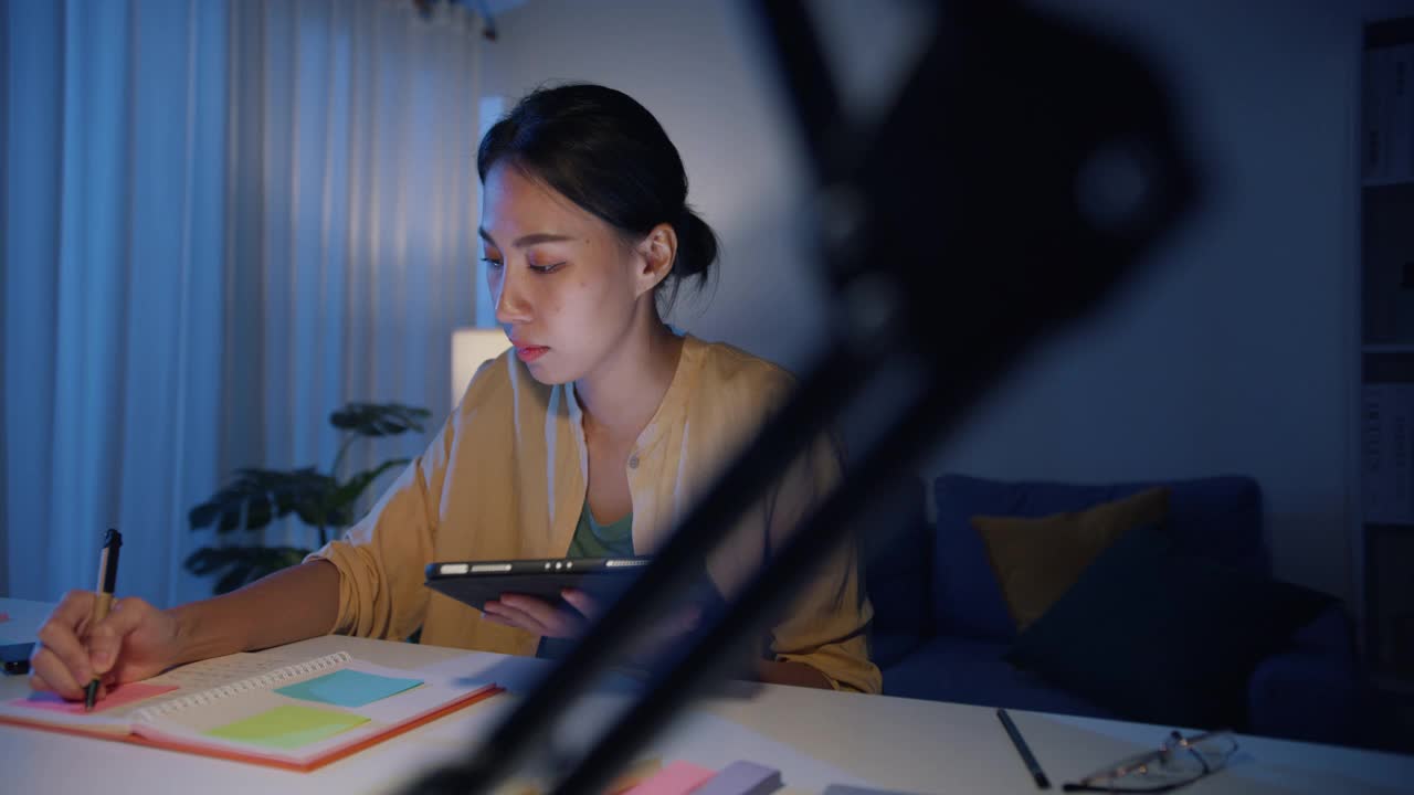亚洲职业女性，穿着休闲服装，晚上在家客厅用平板电脑工作。