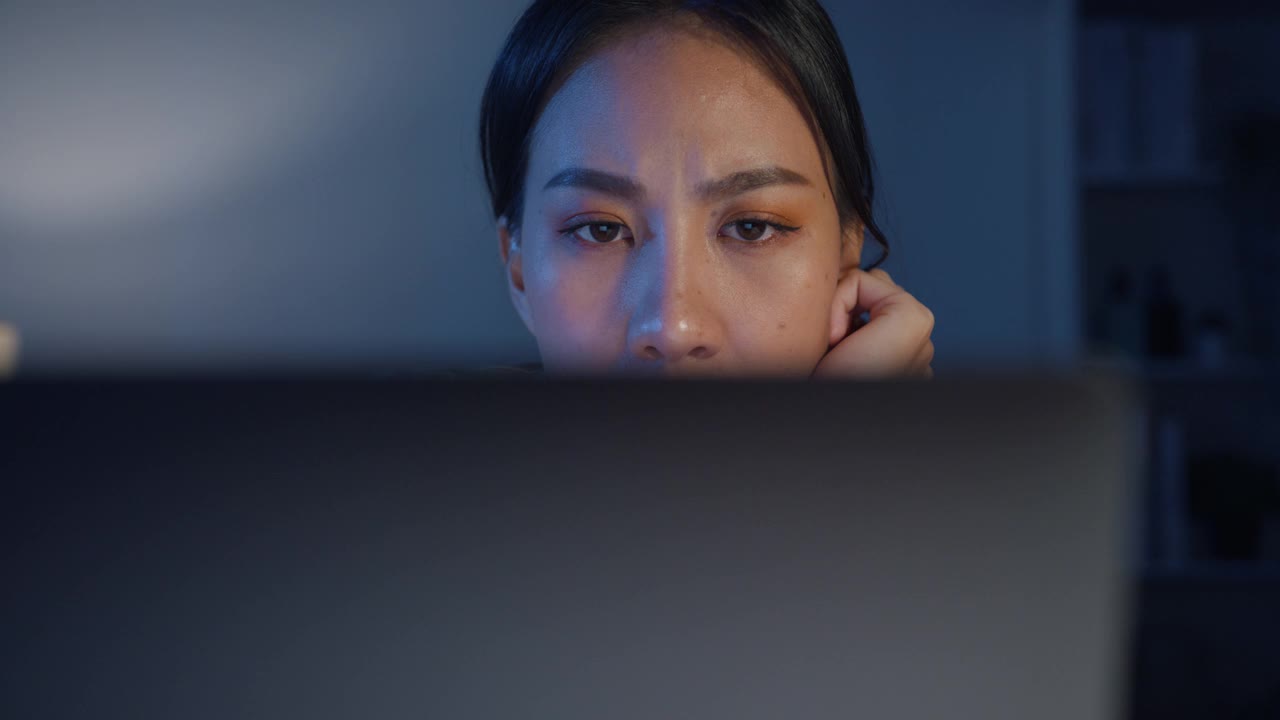疲惫的年轻亚洲商务女性，穿着休闲服装，在家中客厅用笔记本电脑工作。