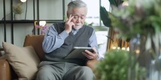 亚洲老年人养老退休老人手用平板电脑冲浪社交媒体浏览朋友在线社交沟通距离连接，幸福亚洲老人呆在家里使用平板设备在家