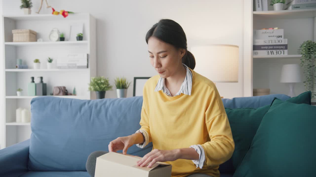 年轻女子在家中客厅沙发上打开纸箱收包裹。