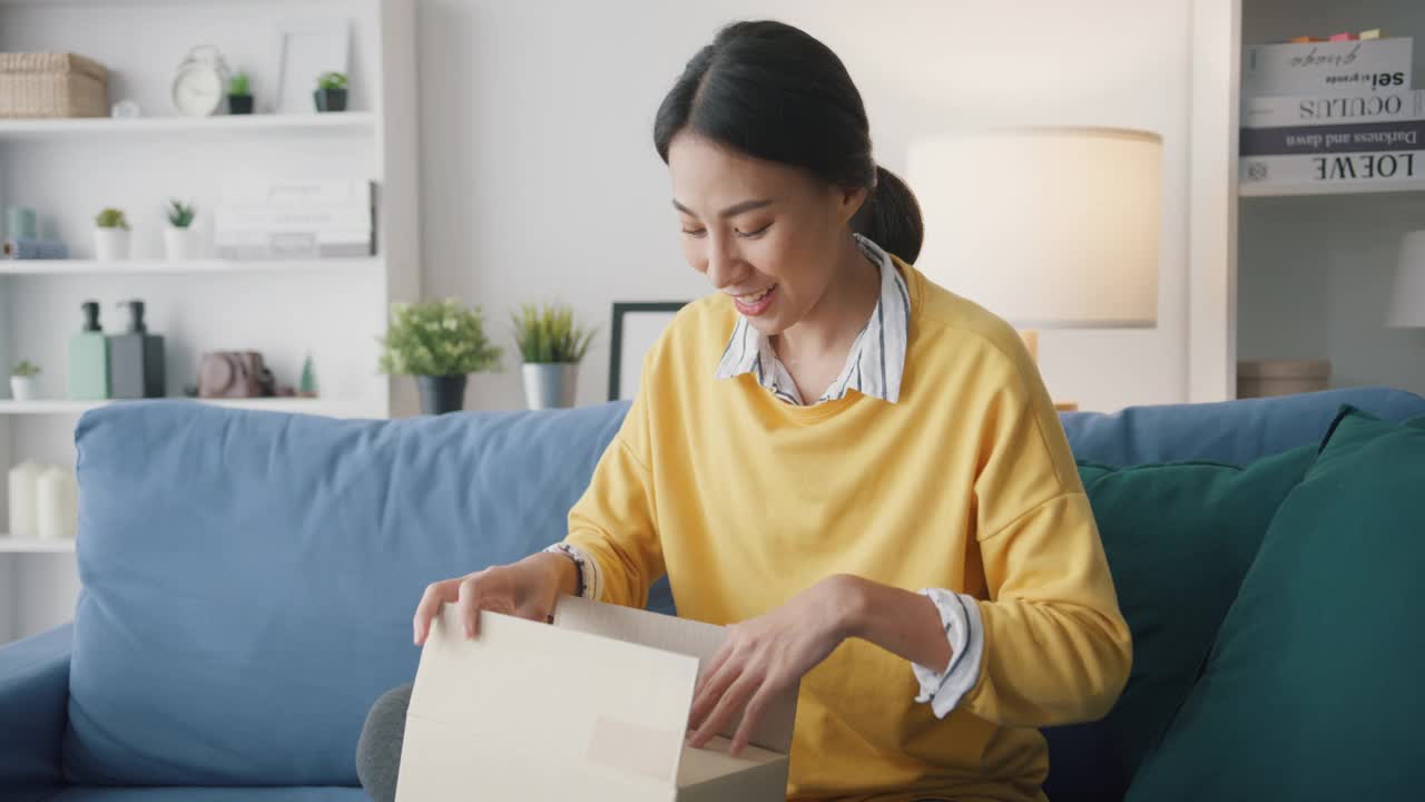 年轻女子在家中客厅沙发上打开纸箱收包裹。
