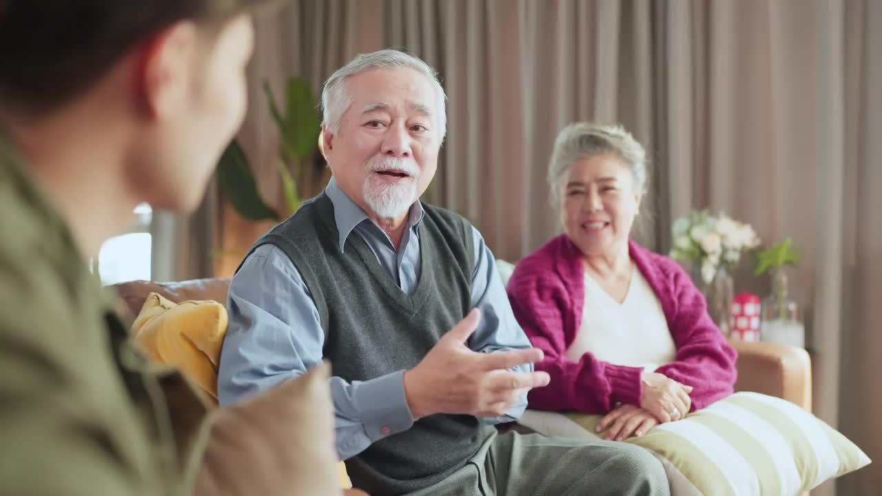 年轻的亚洲男性儿子在家中客厅交谈并把圣诞礼物盒送给祖父母，年老的亚洲退休夫妇留在家中与家人一起欢度节日