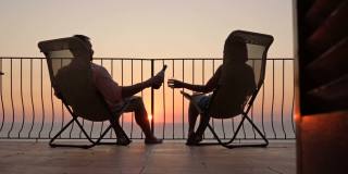美丽的年轻夫妇在露台上喝葡萄酒，欣赏海上的日落