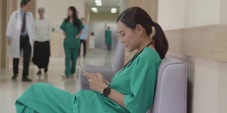 在现代医院里，穿着手术服的女护士下班后用智能手机放松，坐在走廊的沙发上。诊所里，快乐的女医生在智能手机屏幕上滚动。