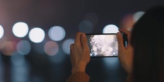 女人用手机拍摄夜空烟花的画面。