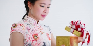 特写:中国/亚洲妇女穿着旗袍白色的衣服打开一个金色的大礼盒，在她的家人，亲戚和朋友的新年快乐，在中国的新年节日