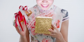 正面特写:中国/亚洲妇女打开她手中的一个金色的大礼盒，她从她的家人，亲戚和朋友的新年快乐，在中国的新年节日，穿着旗袍白色的衣服