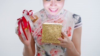 正面特写:中国/亚洲妇女打开她手中的一个金色的大礼盒，她从她的家人，亲戚和朋友的新年快乐，在中国的新年节日，穿着旗袍白色的衣服视频素材模板下载