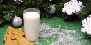人造雪花飘落在圣诞饼干、一杯牛奶和圣诞装饰品上。给圣诞老人的圣诞礼物。全高清