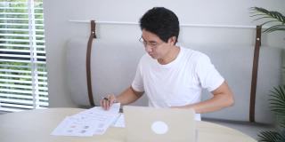 亚洲男性自由职业者使用笔记本电脑在家里的客厅工作