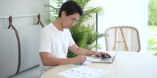 亚洲男性自由职业者使用笔记本电脑在家里的客厅工作