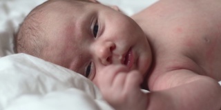 新生儿在白色毯子上的特写肖像。软的焦点。婴儿侧身躺着。1、2周大。小女孩在家里的床上醒来。新的生活和成长观念。真实的人。
