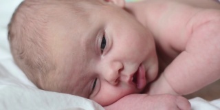 新生儿在白色毯子上的特写肖像。软的焦点。婴儿侧身躺着。1、2周大。小女孩在家里的床上醒来。新的生活和成长观念。真实的人。