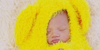 快乐的新生儿断奶可爱的黄色鸡蛋服装躺在灰色的地毯背景睡觉舒适和安全。可爱的亚洲婴儿在婴儿床上睡觉和打盹。新生儿复活节概念