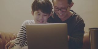 亚洲父亲和儿子坐在房间里一起看笔记本电脑