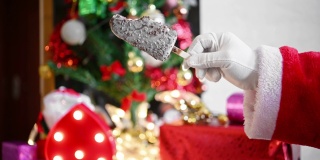 圣诞老人在家里的圣诞装饰前举起一根巧克力冰棒咬一口