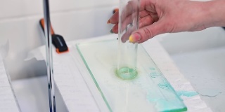 玻璃管将水倒在尿布材料上。研究人员的手正对玻璃管的位置。尿不湿布料及其吸收能力的检查。