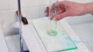玻璃管将水倒在尿布材料上。研究人员的手正对玻璃管的位置。尿不湿布料及其吸收能力的检查。视频素材模板下载