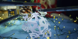 高精度手术设备的机械臂握住纸雪花，切成小片。模糊的圣诞装饰和背景灯光。关闭了。