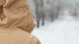 从离焦到离焦。成熟的女人穿着黄色的冬季夹克，头戴兜帽，走在雪地里的公园里。视频素材模板下载