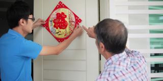 亚洲华人的儿子和父亲在中国新年前夕用“财运”春联装饰他的房子
