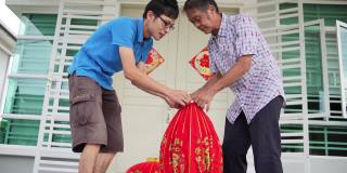 亚洲华人父亲和儿子准备大红灯笼在他们家的前院在中国新年前夕