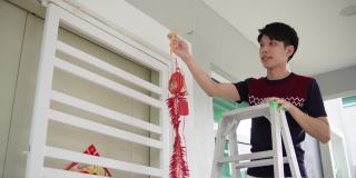 亚洲华人微笑的男性挂现代鞭炮在他的房子前在中国新年前夕