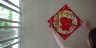 亚洲的中国妇女在中国新年前夕用“财运”春联装饰她的房子