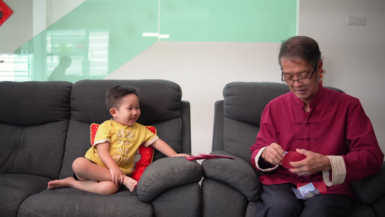 亚洲华人微笑可爱的孙子看着爷爷，而他在春节期间在生活大厅装红包