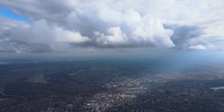 从高空的飞机窗口鸟瞰，远处的城市被暴雨前形成的蓬松的积云所覆盖