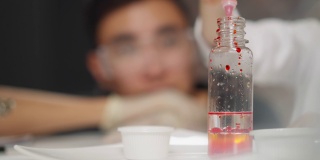 在化学测试中，女孩将红色颜料滴入透明液体中