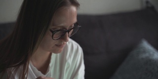 一名女子在一个多云的清晨坐在家里的沙发上用笔记本电脑工作。她看着电脑屏幕，在键盘上打字。在家工作，学习，流行病
